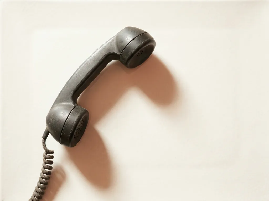 Vintage zwarte telefoonhoorn op wit oppervlak, licht van de haak, met zachte schaduw in minimalistische flatlay-compositie.