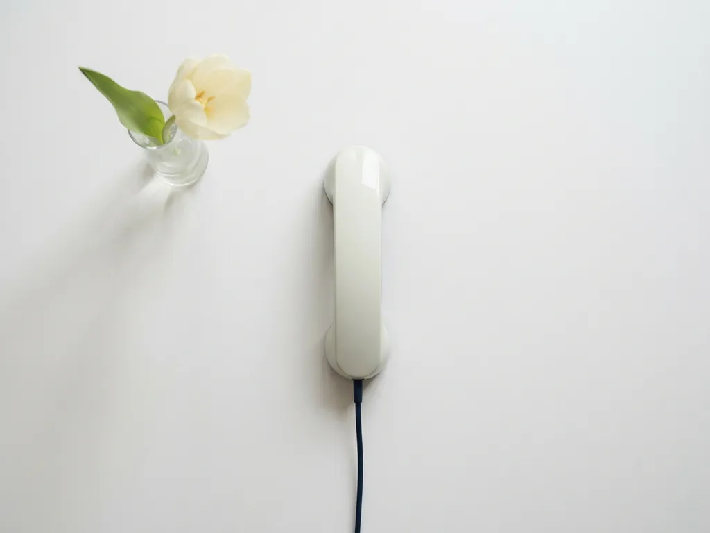 Stijlvolle telefoonhoorn op wit oppervlak naast een verse tulp, minimalistische compositie in ivoor- en marineblauw tinten.