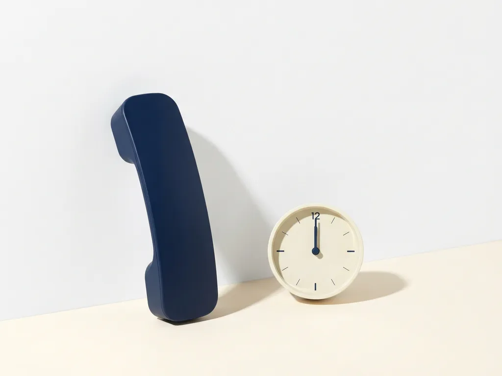 Zwarte telefoonhoorn op wit oppervlak naast analoge klok die middernacht aanwijst, minimalistische compositie in ivoor en marineblauw.